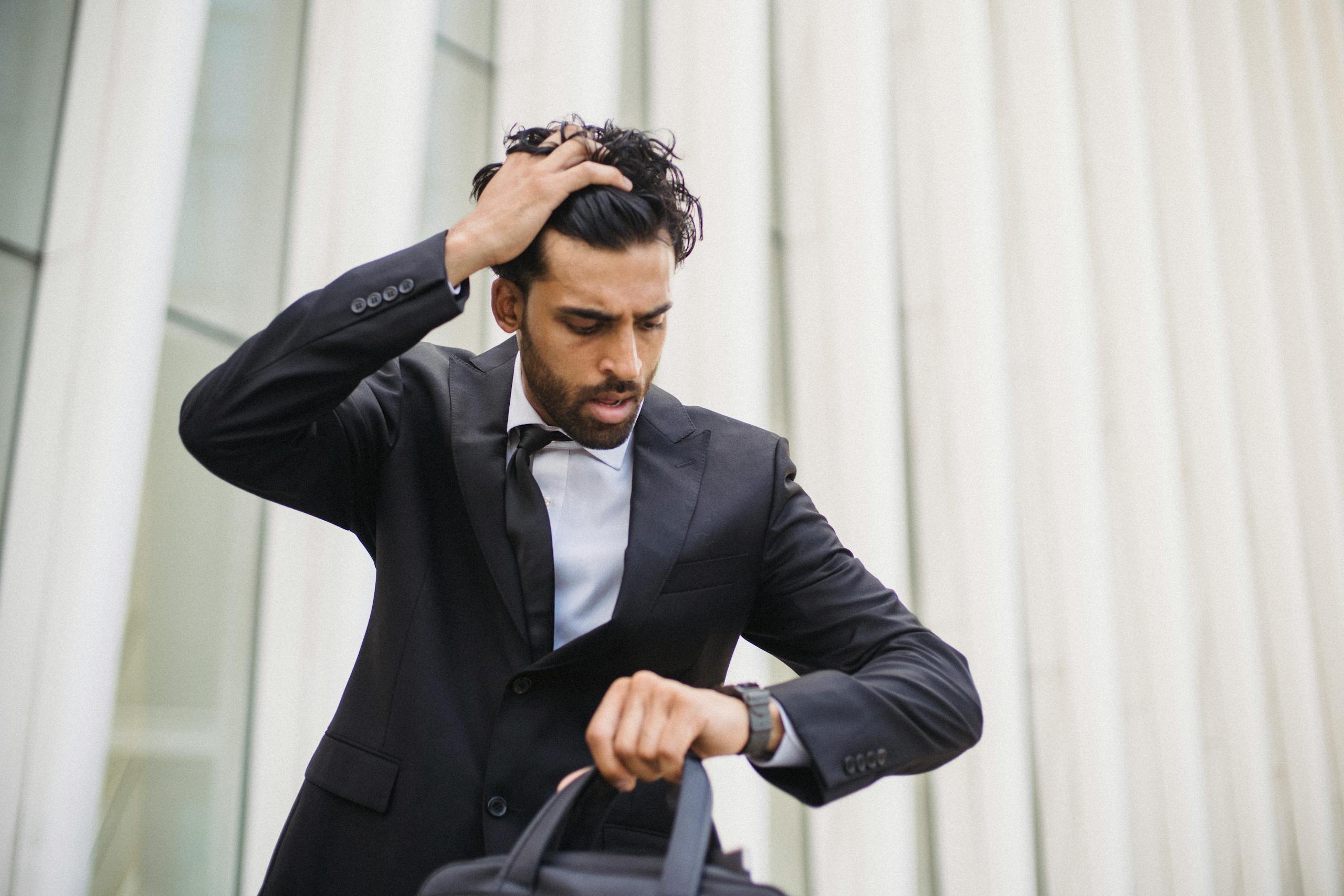A businessman in a suit checks his watch, expressing stress. Suitable for business themes.