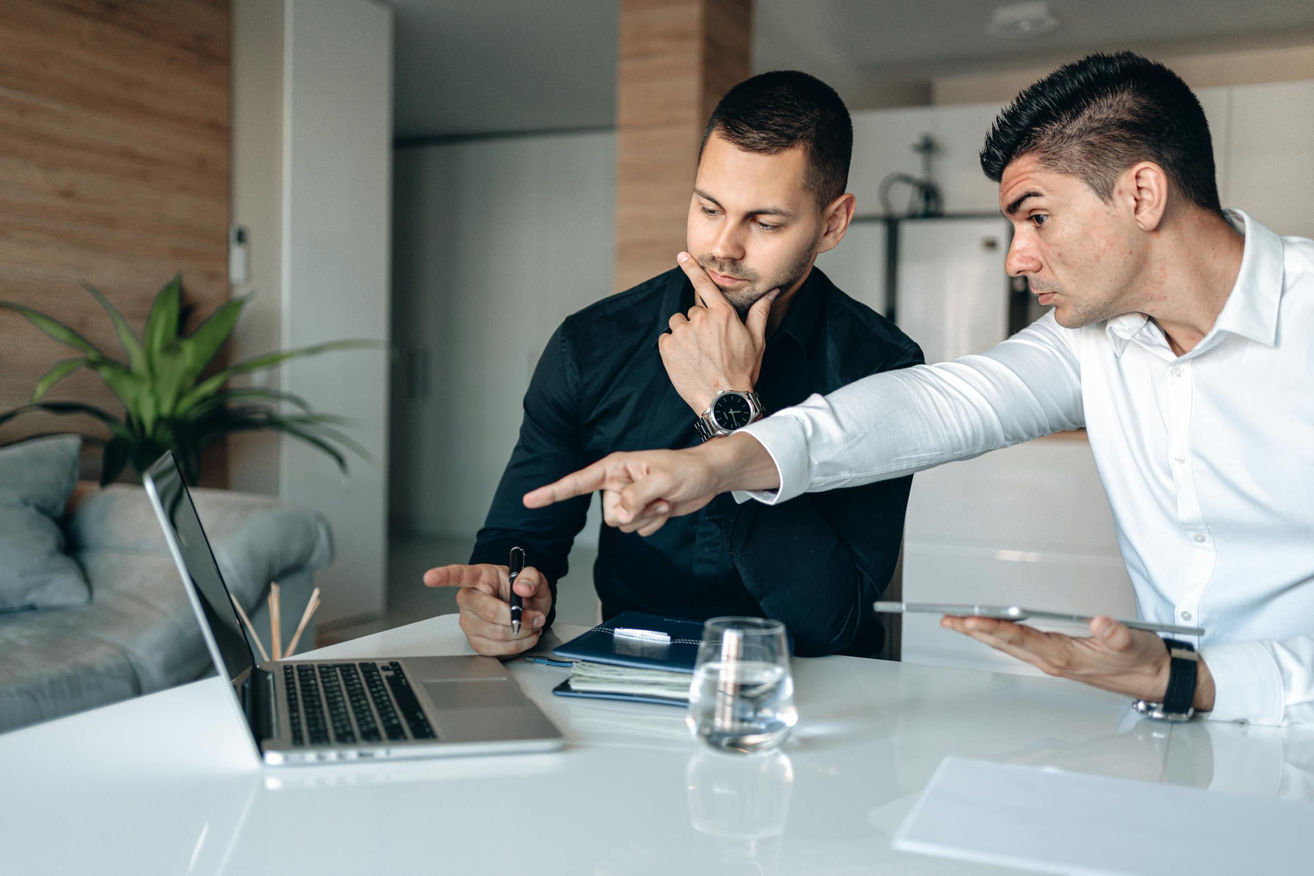 Two men in an office intensely focusing on a laptop while discussing a business project.